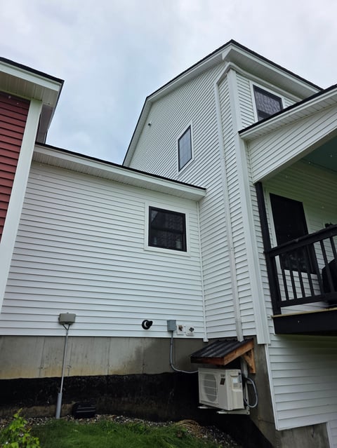 Two-story white house with dark roof and black deck, viewed from exterior showing siding, windows, and foundation