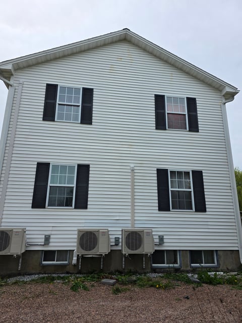 Two-story white house with black shutters, four front windows, and three air conditioning units at ground level