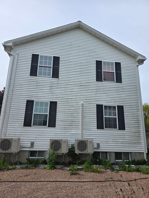Two-story white house with black shutters, multiple windows, and air conditioning units at the foundation
