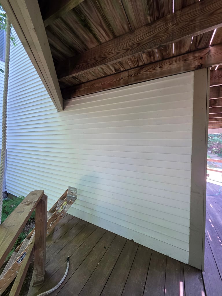 Interior view of a covered porch with white horizontal siding wall and exposed wooden beam ceiling